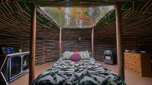 A room with a bed, a small table, a speaker, and a wall with a naturalistic design.