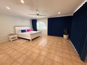 A bedroom with a bed, a nightstand, a ceiling fan, a window with curtains, and a potted plant. - Entire 4-Bedroom Home — Convenient Access to Brisbane and the Gold Coast (Springwood)