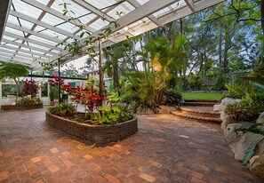 Eine überdachte Terrasse mit Backsteinboden, verschiedenen Pflanzen und Blick auf die umliegende Natur.