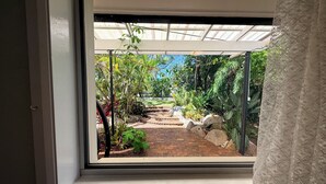 Ein Fenster mit Blick auf einen Garten, darunter ein Pflasterweg und verschiedene Pflanzen.