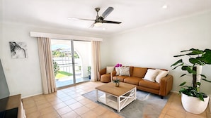 Ein Wohnzimmer mit einer Couch, Couchtisch, Deckenventilator und einem großen Fenster mit Vorhängen.