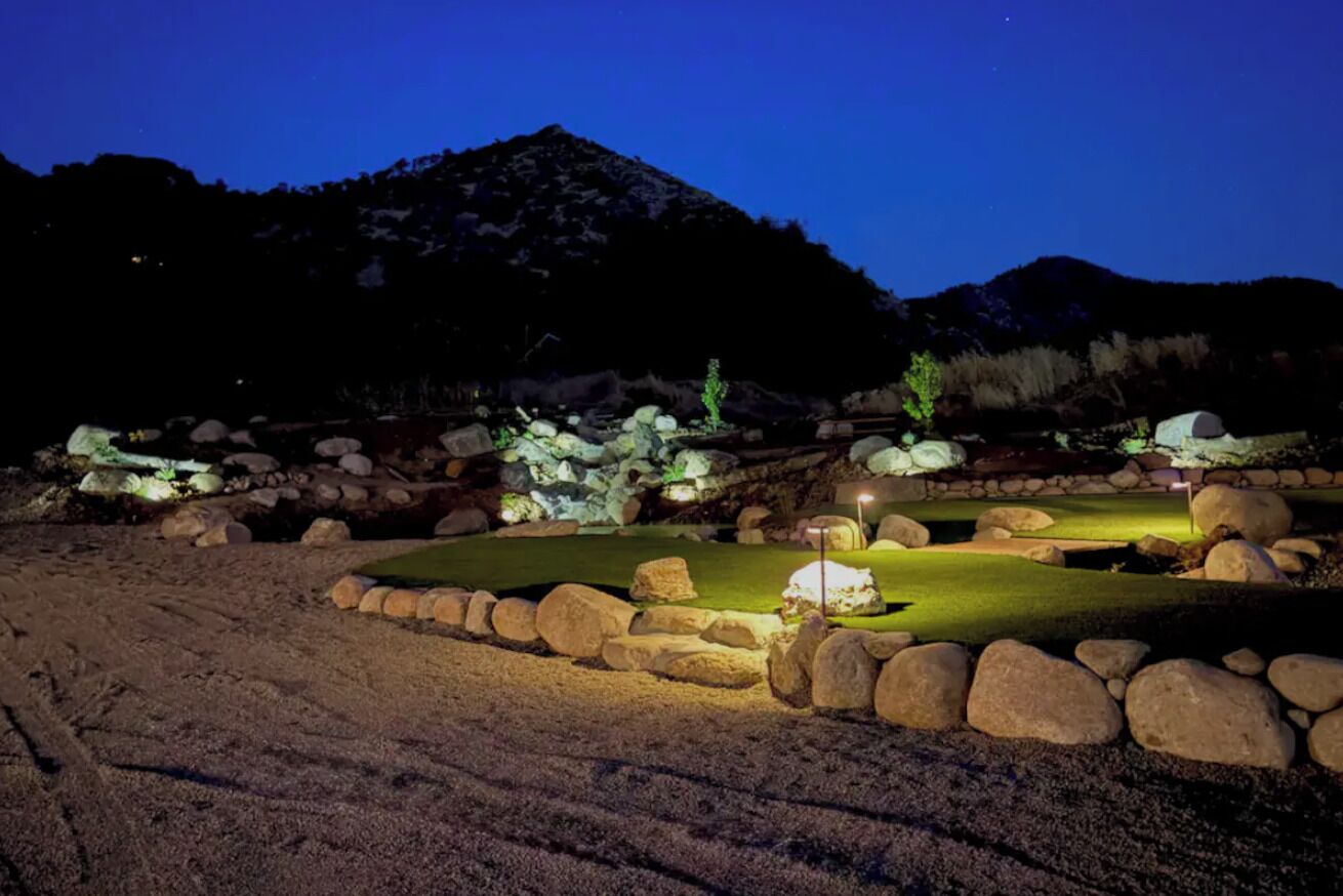 Een golfbaan 's nachts met verlichte paden, een putting green en omliggende rotsen.