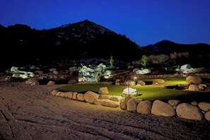 Een golfbaan 's nachts met verlichte paden, een putting green en omliggende rotsen.