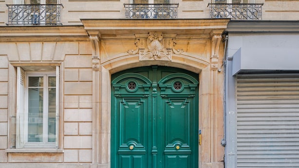 Eine Gebäudefassade mit einer grünen Doppeltür, einem Fenster links und einem geschlossenen Garagentor rechts.