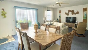 Uma sala de estar com uma mesa de jantar, cadeiras, uma televisão e um ventilador de teto.