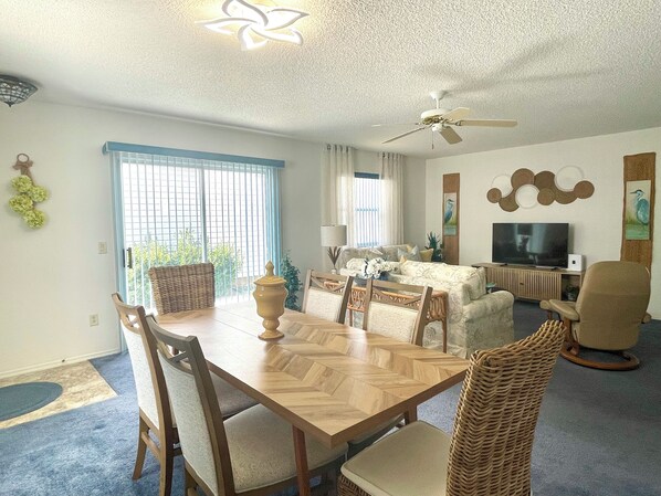 A living room with a dining table, chairs, a TV, and a ceiling fan.