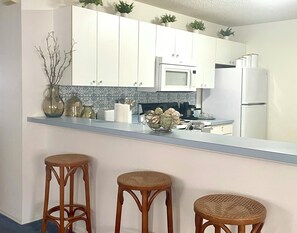 A kitchen with white cabinets, a microwave, a refrigerator, and three wicker stools.