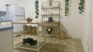 Uma cozinha com geladeira branca, mesa de madeira, estante de metal e piso ladrilhado.