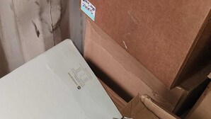 A hand holding a binder with a white sheet of paper inside, placed on a cardboard box.