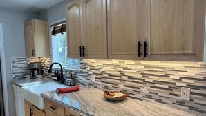 A kitchen with wooden cabinets, a marble countertop, and a tiled backsplash. - Peaceful Shaver Lake Mountain Retreat with Deck & Forest Views (Shaver Lake)