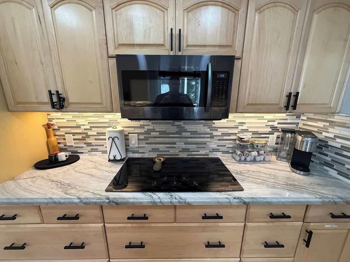 A kitchen with wooden cabinets, a black microwave, a gas stove, and a marble countertop.
