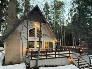 Mökki, jossa on terassi, ja sen ympärillä on puita. Lisäksi siellä on laituri, joka ulottuu vesistöön.
