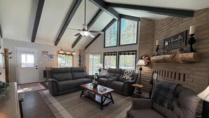 A spacious living room with a fireplace, large windows, and a ceiling fan. - Peaceful Shaver Lake Mountain Retreat with Deck & Forest Views (Shaver Lake)