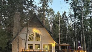 A cabin with a wooden deck, a staircase leading to the entrance, and a large window. - Peaceful Shaver Lake Mountain Retreat with Deck & Forest Views (Shaver Lake)