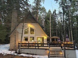Eine Holzhütte mit einer Holzterrasse, einer Treppe, die zum Eingang führt, und einem großen Fenster.