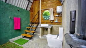 A compact bathroom with a toilet, sink, and a small window with a view of greenery.