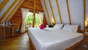 A single bedroom with a wooden ceiling, a bed with white linens, a nightstand, a chair, and a window with curtains.