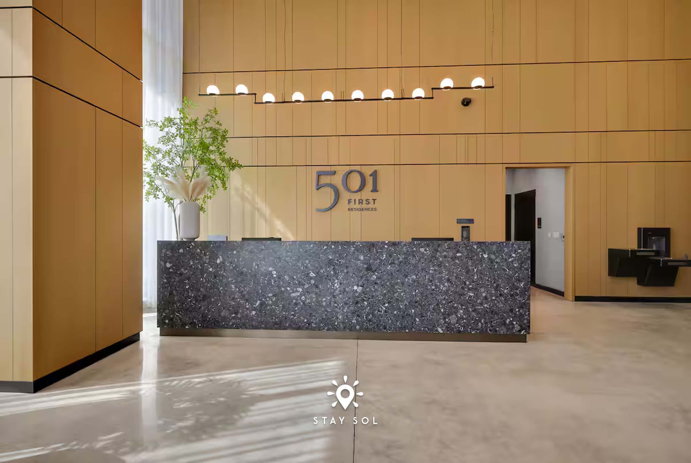 A reception desk with a sign reading '501 First Residences,' a plant, and a modern interior design.