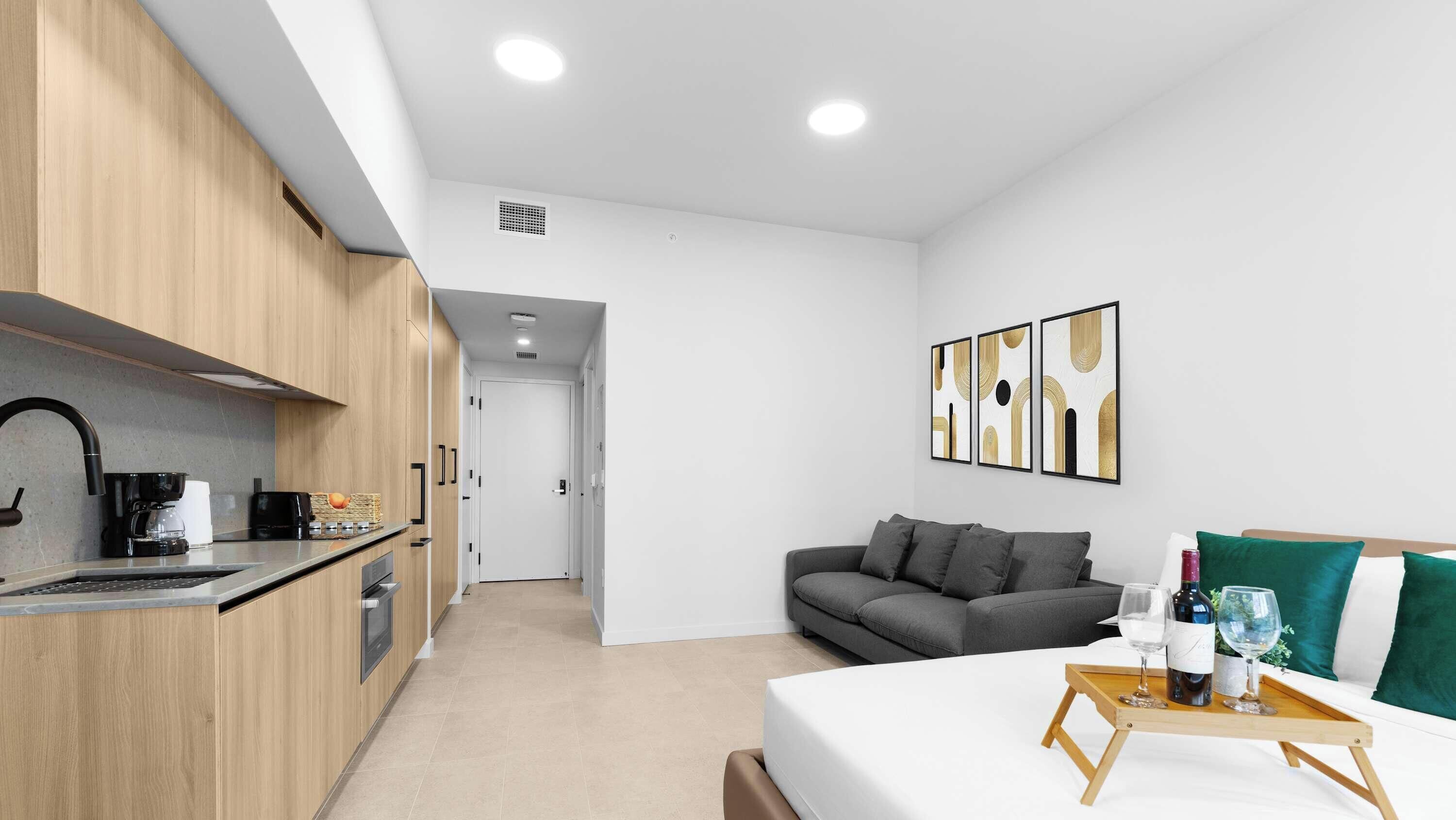 A modern kitchen with a coffee maker, a dining area with a table set for two, and a gray sofa.