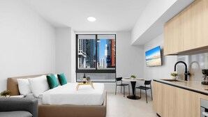 Een moderne hotelkamer met een bed, bureau, stoel, klein tafeltje, televisie en een kitchenette.