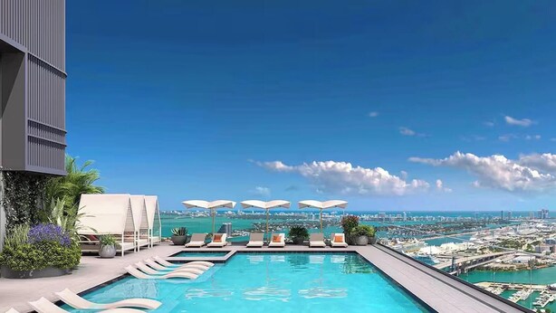 A rooftop infinity pool with lounge chairs and umbrellas, overlooking a cityscape and coastline. - Elite Stay with Rooftop Vibes Studio (Miami)