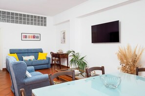 A living room with a sofa, dining table, chairs, a TV, and a potted plant. - Panoramic Sea-View Terrace in the Quiet Beauty of the Sorrento Coast (Massa Lubrense)