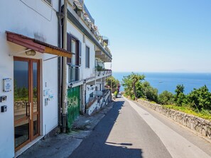 Une rue étroite, bordée d’un bâtiment d’un côté et d’un mur de pierre de l’autre, offrant une vue dégagée sur la mer.