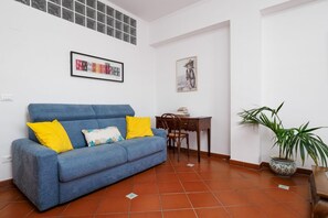 Ein Wohnzimmer mit einem blauen Sofa, einem Esstisch, einem Sessel und einer Topfpflanze.