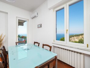 Un coin repas avec une table en verre, des chaises, une vue sur la mer et un mur blanc agrémenté d’un climatiseur.