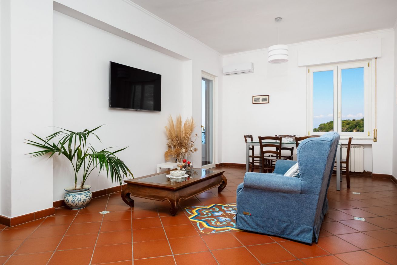A living room with a sofa, a coffee table, a TV, and a dining area with chairs and a table.