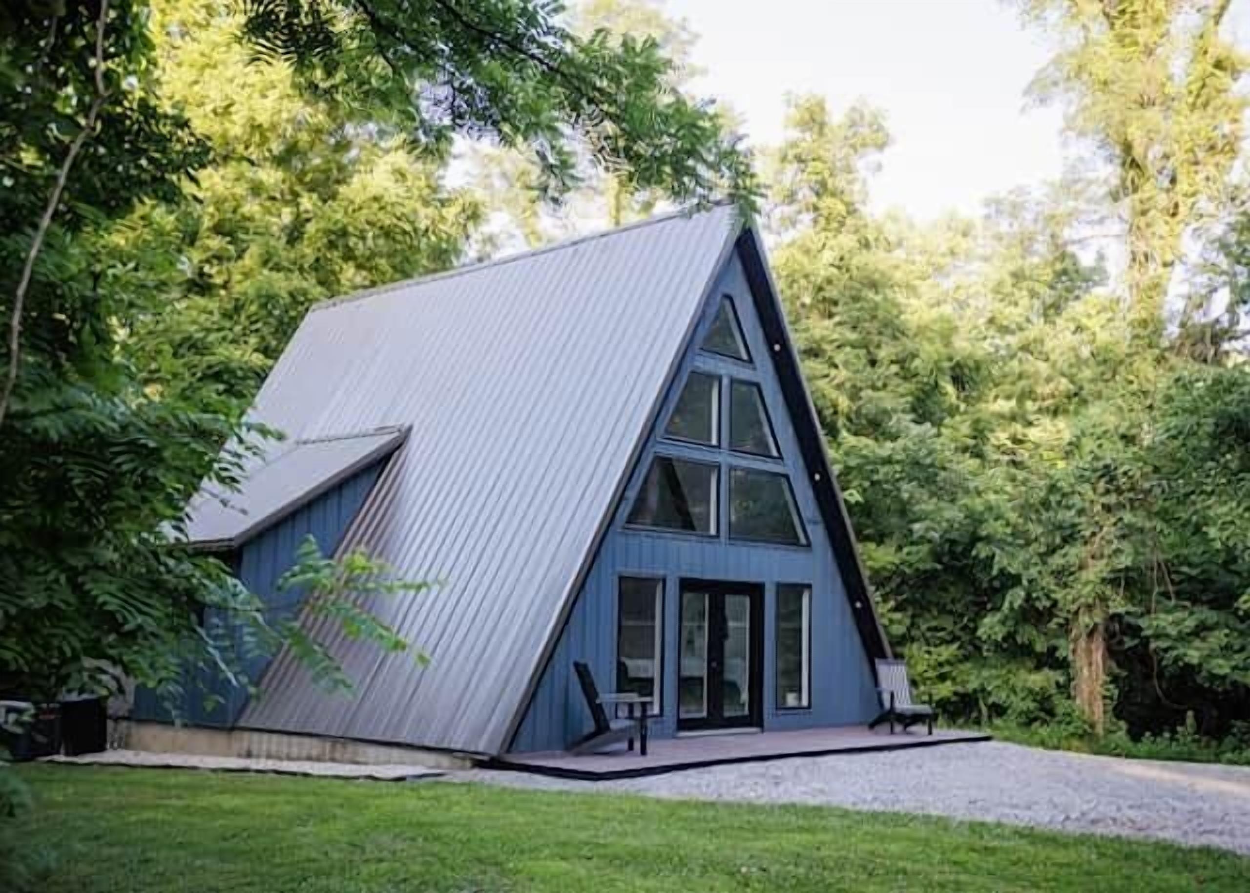 Um edifício em estilo cabana, com telhado metálico azul, rodeado por vegetação.