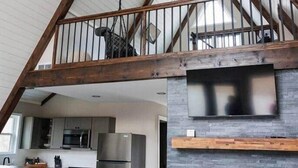 A spacious loft with a high ceiling, exposed wooden beams, a kitchen with modern appliances, and a stone fireplace.
