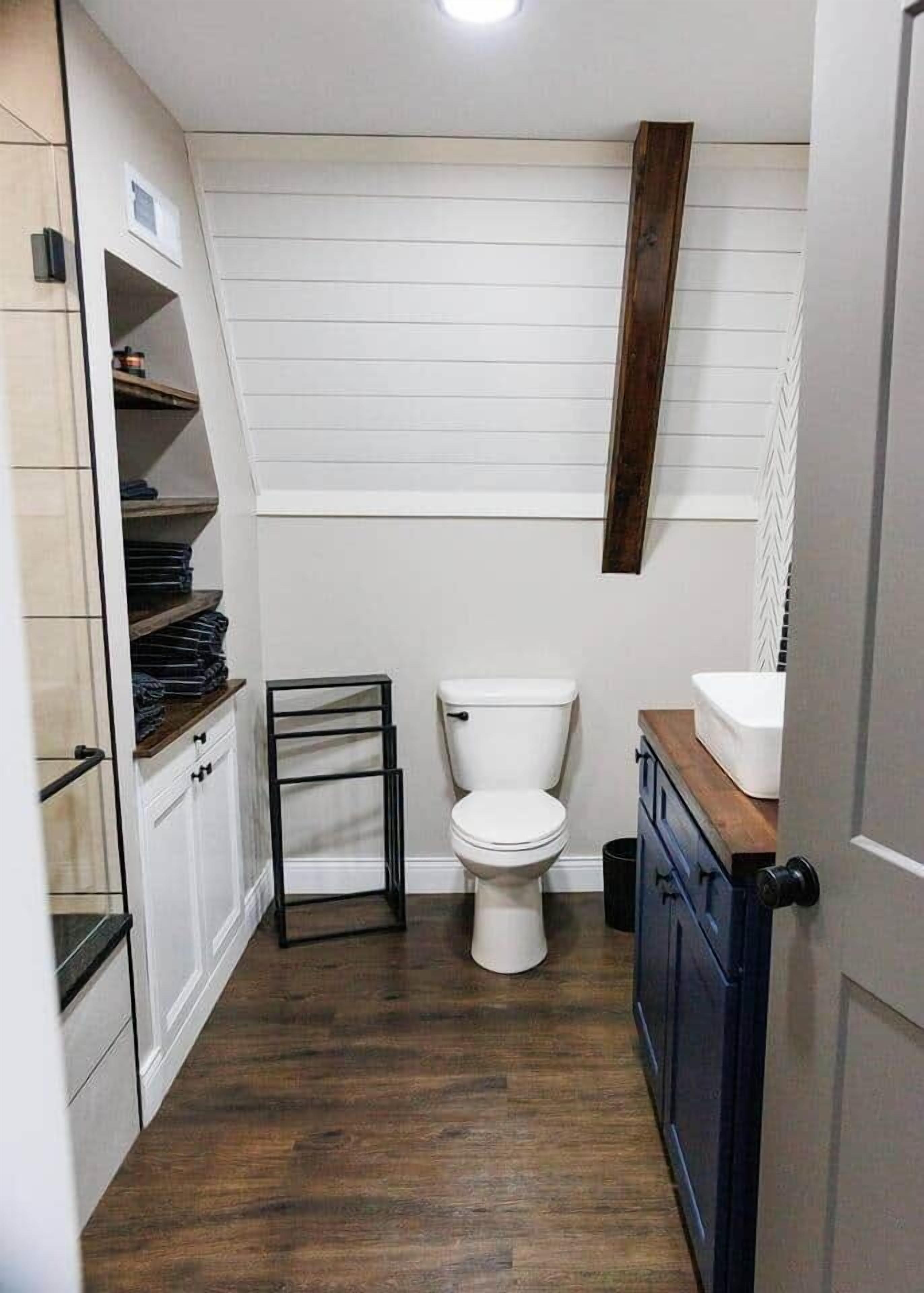 A compact bathroom with a toilet, a small sink, and a wooden shelf unit.