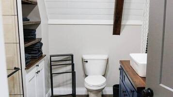A compact bathroom with a toilet, a small sink, and a wooden shelf unit.