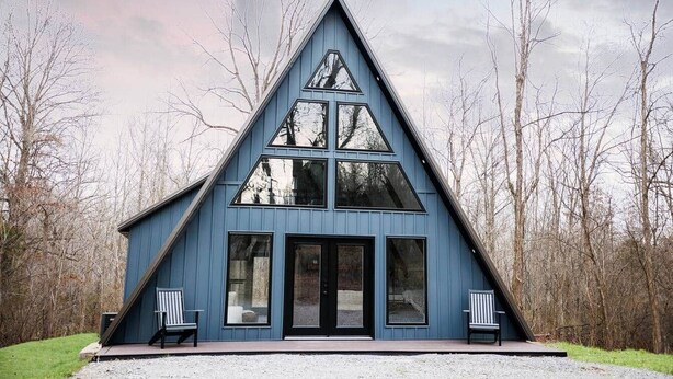 A blue triangular building with a porch, two chairs, and a gravel driveway.