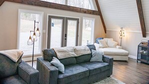 A spacious loft with a high ceiling, large windows, a sectional sofa, and a small side table.