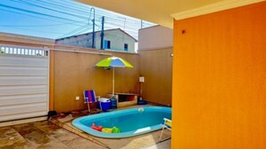 A backyard with a swimming pool, a covered patio area, and a view of neighboring buildings.