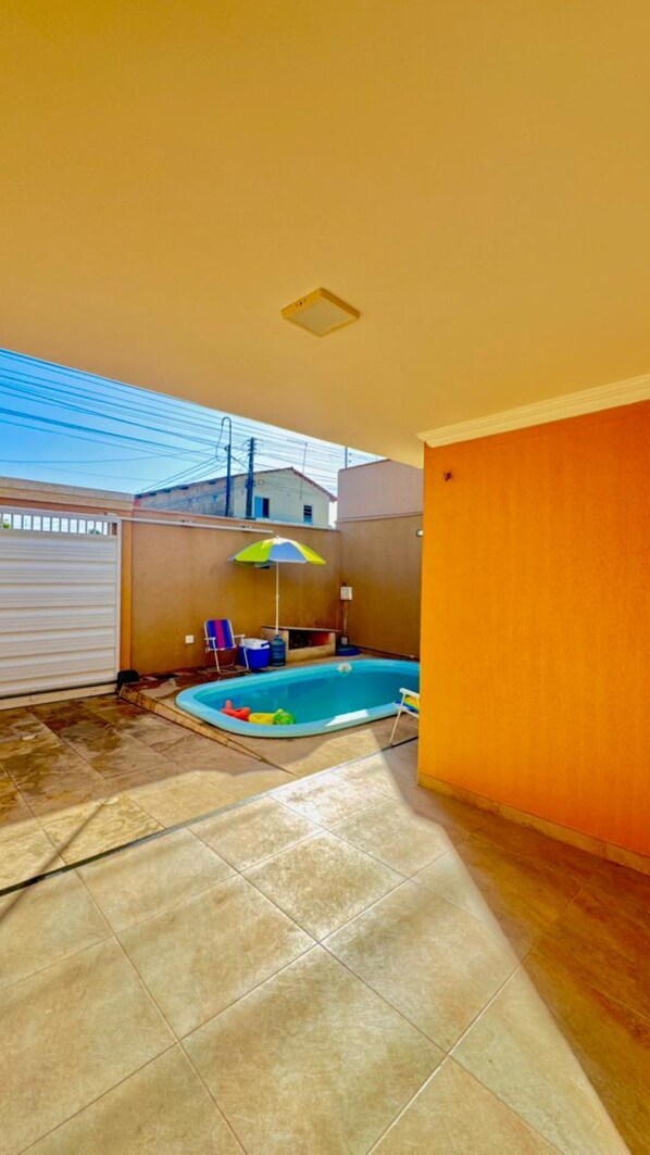 A backyard with a swimming pool, a covered patio area, and a view of neighboring buildings.