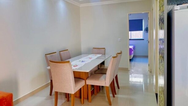 A dining area with a table and chairs, a refrigerator, and a kitchen area in the background.