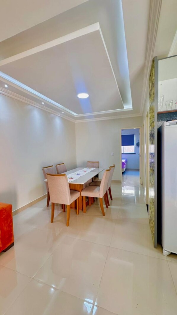 A dining area with a table and chairs, a refrigerator, and a kitchen area in the background.