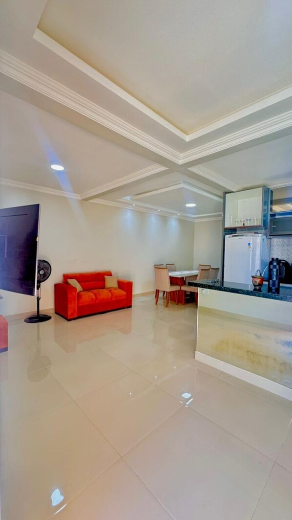 A modern living room with a red sofa, a dining area with a table and chairs, a kitchen with a refrigerator, and a flat-screen TV mounted on the wall. - CASA MARIANNA: Private Pool, 3 Bedrooms & Prime Location in Paracuru (Paracuru)