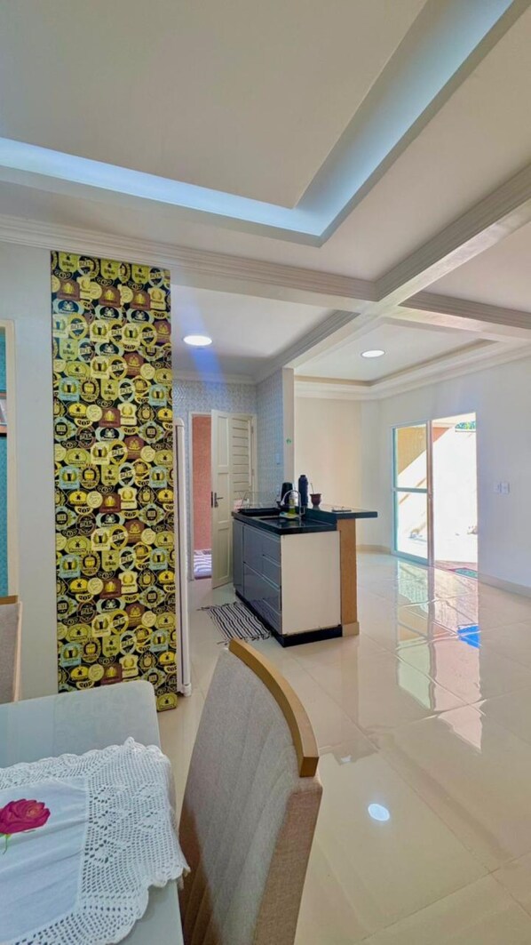 A modern kitchen with a central island, a dining area with a table and chair, and a patterned wall. - CASA MARIANNA: Private Pool, 3 Bedrooms & Prime Location in Paracuru (Paracuru)