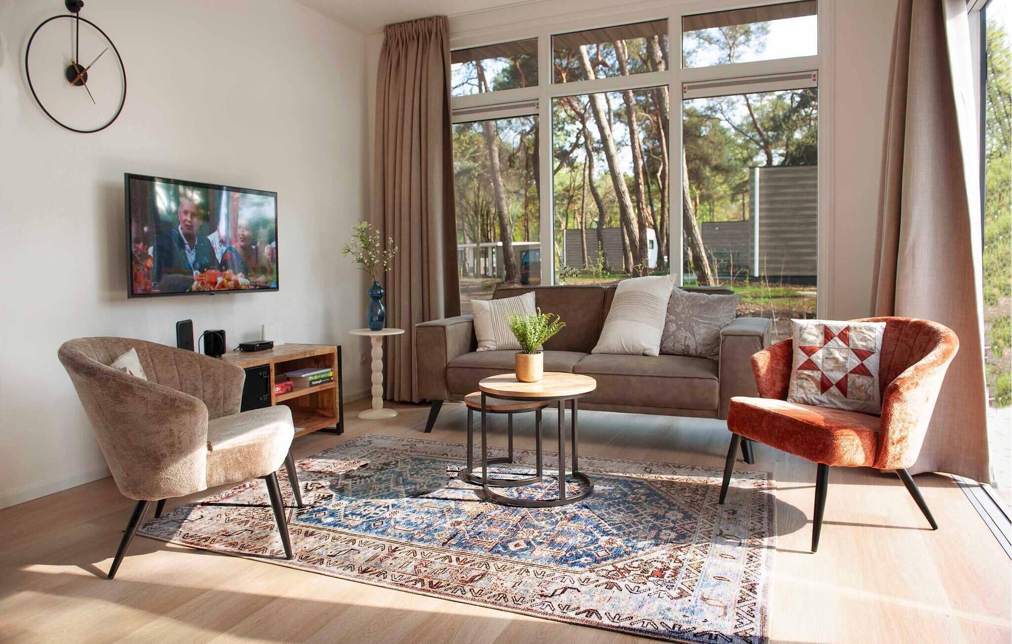 A living room with a sofa, armchairs, a coffee table, a TV, and a window with curtains.