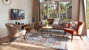 Un salon comprenant un canapé, des fauteuils, une table basse, un téléviseur et une fenêtre avec des rideaux.