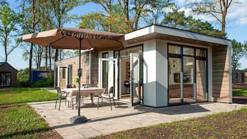 A modern outdoor seating area with a table and chairs, a covered umbrella, and a glass-enclosed structure.
