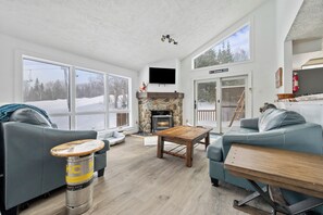 A cozy living room with a stone fireplace, large windows, and a view of the outside. - Saddleback | Rock Pond 34 | Ski in/out | Pet friendly (Rangeley)