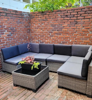 A corner seating area with a brick wall, a woven sofa, and a square table with a plant. - Honey Studio · FIFA Midtown Gem · Private Parking (Atlanta)