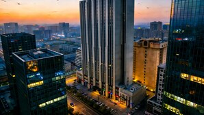 A high-rise building with a modern design, surrounded by other tall buildings, and a clear sky with birds flying. - Chengdu Suli Travel Hotel (Chengdu)
