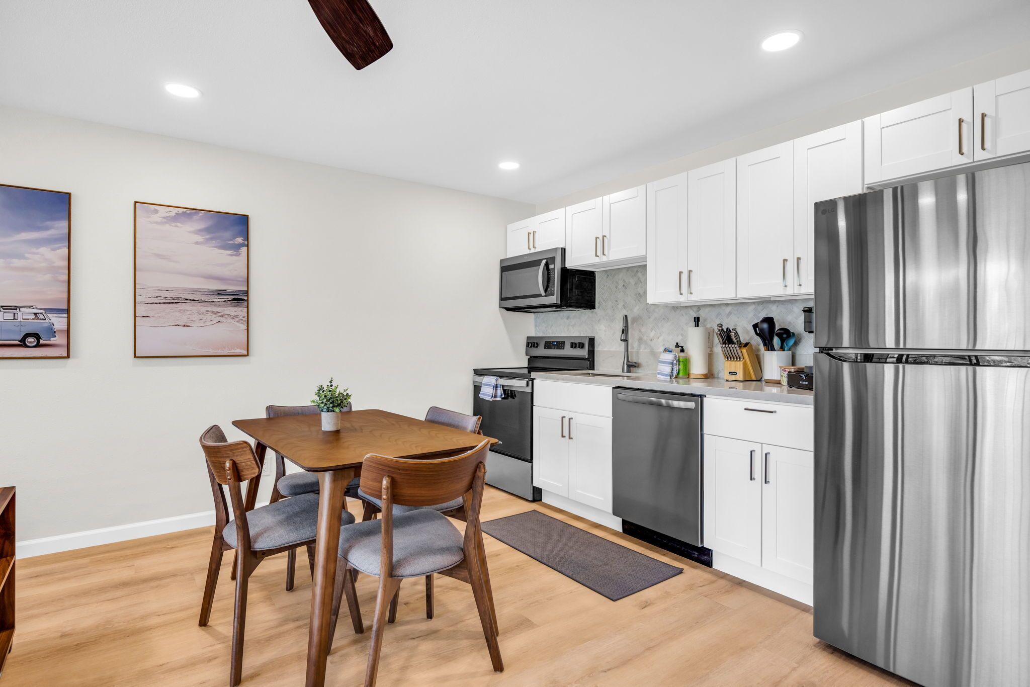 A modern kitchen with white cabinets, stainless steel appliances, and a dining area with wooden furniture.