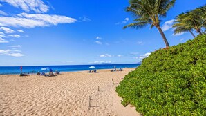 A sandy beach with palm trees, umbrellas, and people. -  Kihei Kai Nani Beachside Resort Vistas (Kihei)